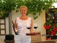 Martina Schuh hält eine Flasche und ein Tablett mit 2 Gläsern Rotwein