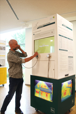 Männliche Person steht vor einem Ausstellungsobjekt mit einem Hörer in der Hand.