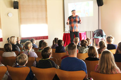 viele Kinder sitzen vor der Bühne und schauen zum Autor nach vorn