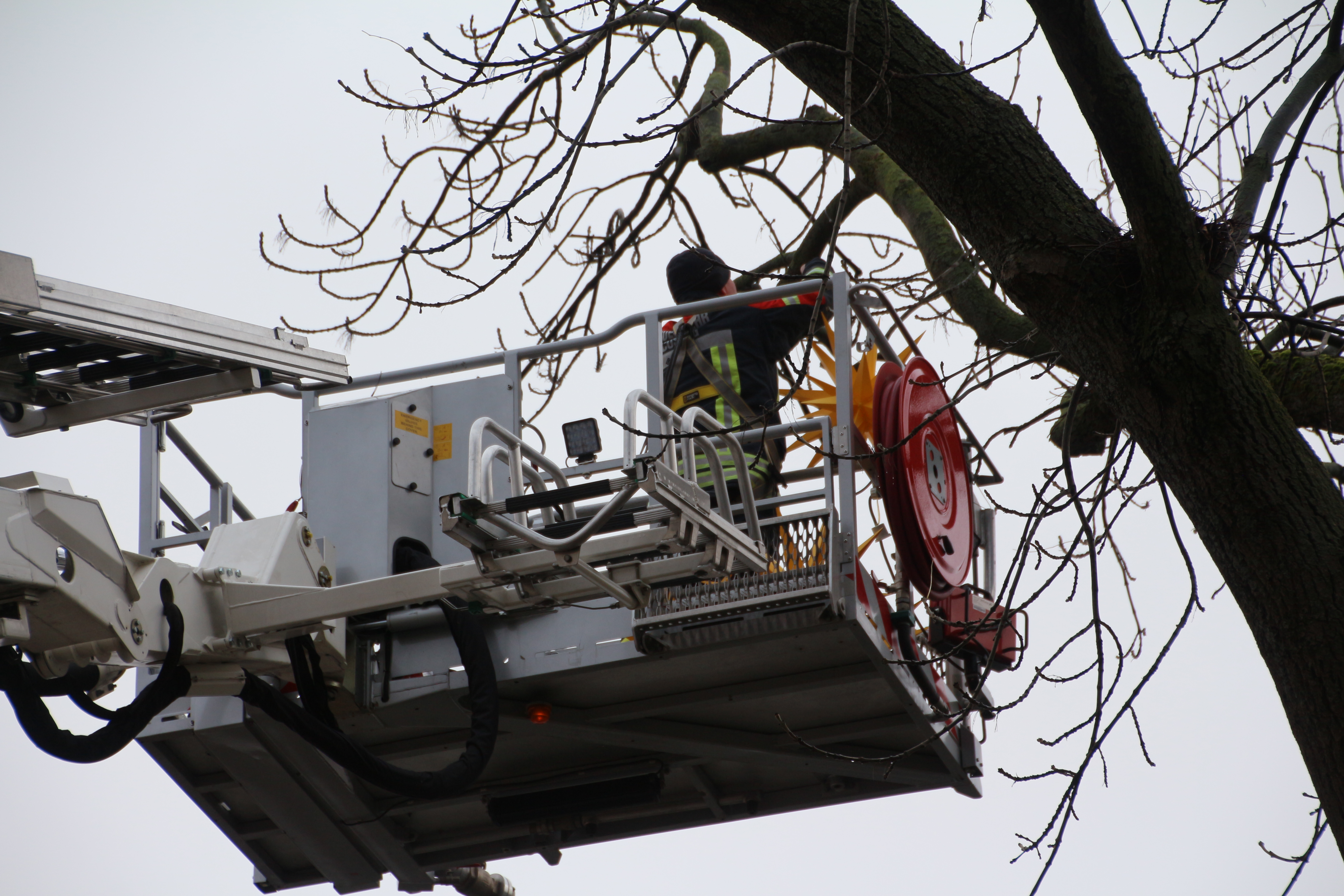 Feuerwehrmann steht im Korb der Drehleiter und hängt Weihnachtssterne auf