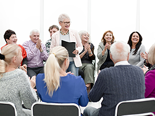 Senioren sitzen im Kreis und klatschen Vortragender zu
