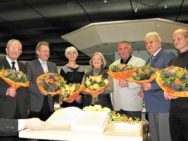 Langjährige Stadträte mit Blumenstrauß stehen hinter einem Tisch mit aufgeklapptem Ehrenbuch